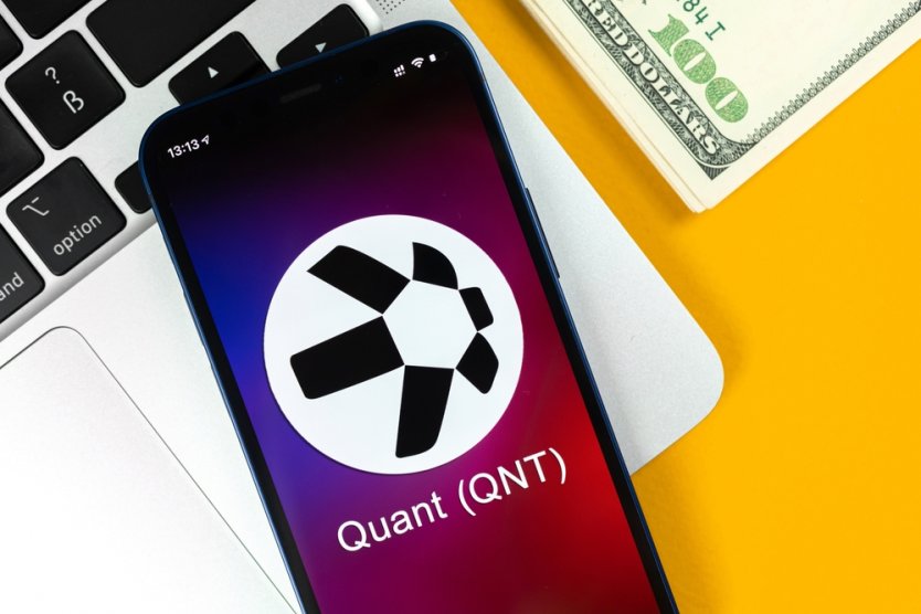 A mobile phone displays the logo, name and ticker for Quant (QNT)