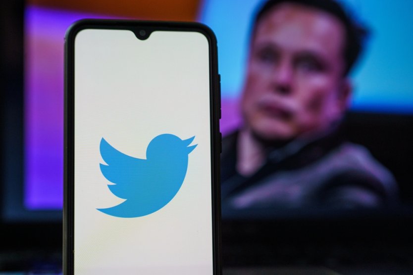  Twitter logo on smartphone and Elon Musk in the background