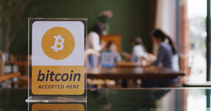 A sign reading “bitcoin accepted here” is displayed on a counter in a coffee shop 
