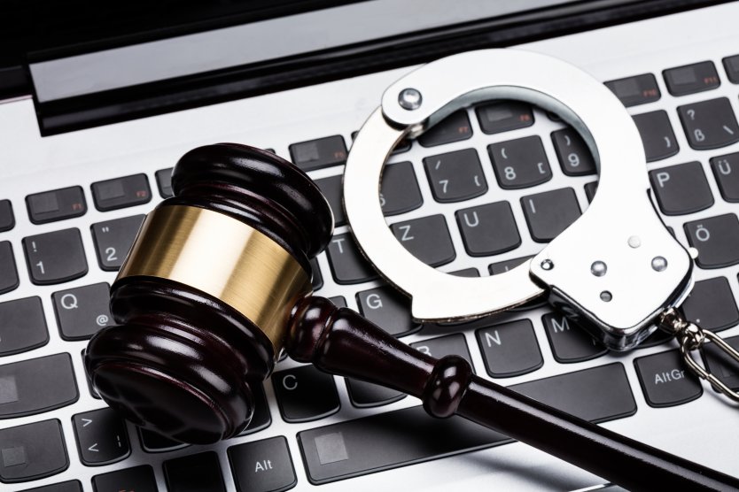 A laptop keyboard with a set of handcuffs and a judge’s gavel