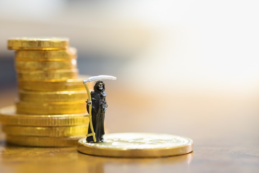 Grim reaper figurine beside a pile of coins – Photo: Shutterstock