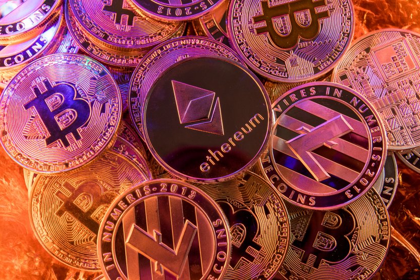 Pile of golden crypto coins including BTC and ETH, under purple, pink and blue mood lighting 